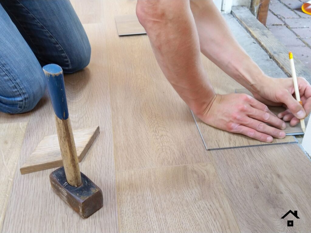 Person marking a wood-look flooring plank to fit around a doorway during installation.
